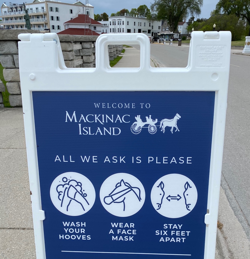 A sign on Mackinac Island that humorously depicts horses wearing masks and social distancing