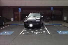 Photograph of black SUV parked fully inside of access aisle between two reserved disability parking spaces.￼